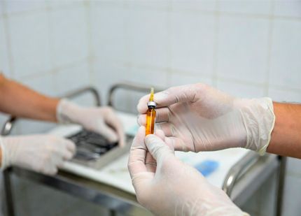 Руки в перчатках держат ампулу с оранжевой жидкостью