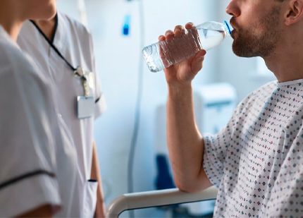 Пациент в больнице пьёт воду из бутылки под присмотром медсестры